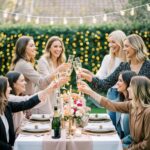 Skupina žen slaví rozlučku se svobodou u venkovního stolu s přípitkem ve večerní zahradě.