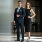 Muž v tmavém obleku a žena v černých šatech stojí v elegantním moderním interiéru.
