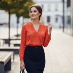 Žena s hruškovitou postavou v barevné blůze a tmavých kalhotách ve městě s moderním pozadím